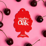 A Cherry Mighty Oak car air freshener surrounded by fresh cherries