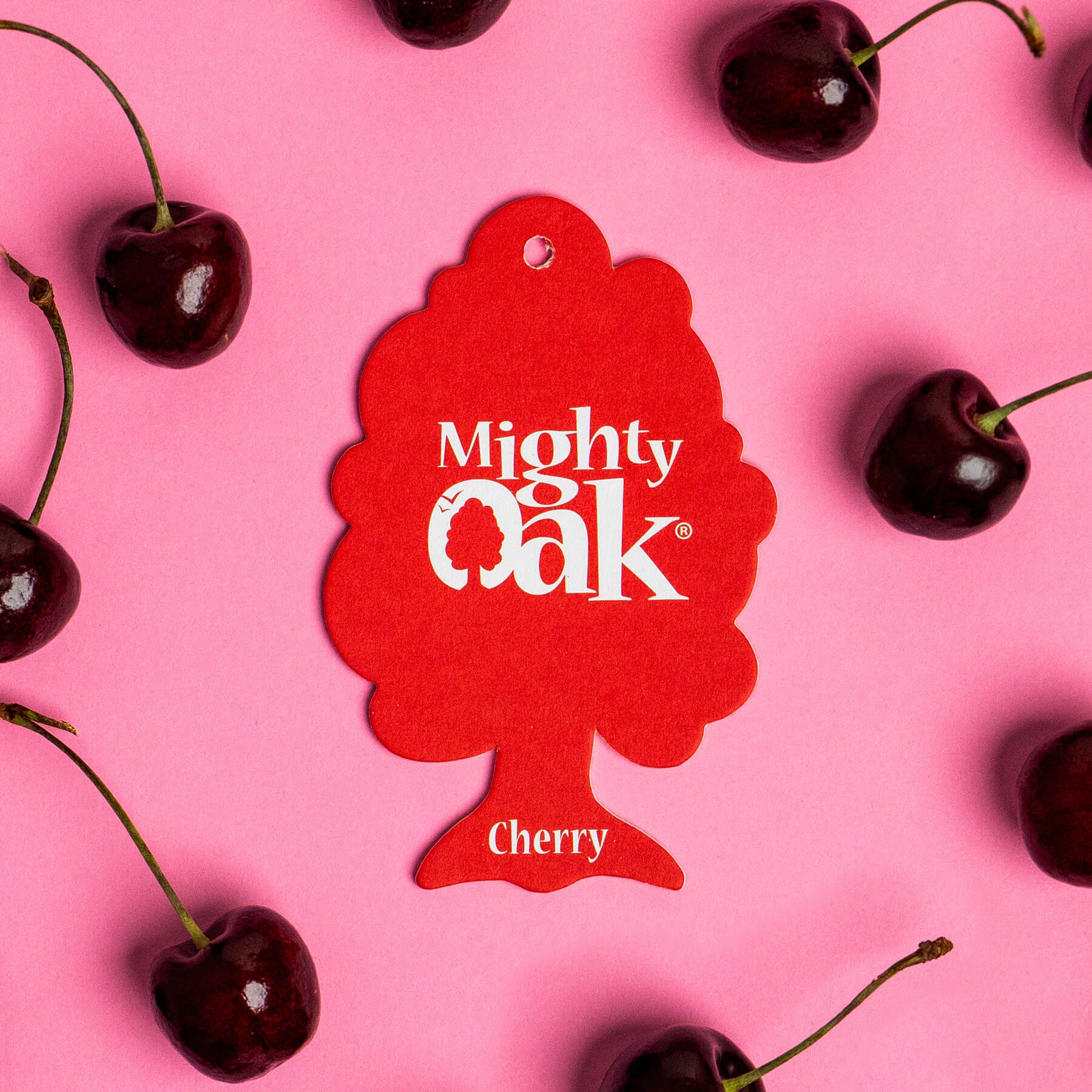 A Cherry Mighty Oak car air freshener surrounded by fresh cherries